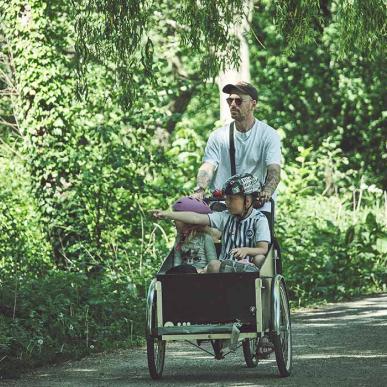 Mand cykler i grønne omgivelser med børn i ladcykel