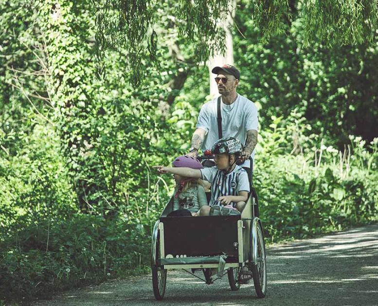 Mand cykler i grønne omgivelser med børn i ladcykel